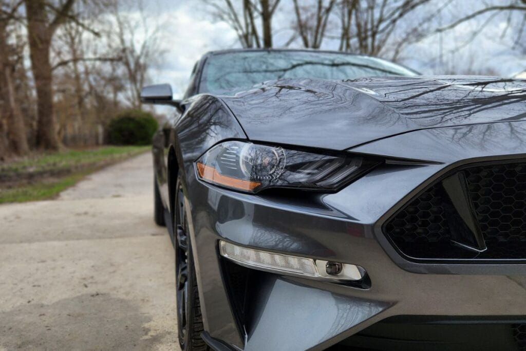 Gray Ford Mustang parked on a paved road with trees in the background.