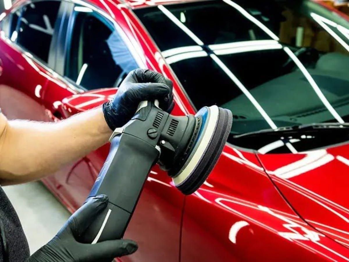 Technician machine polishing a red vehicle before ceramic coating.