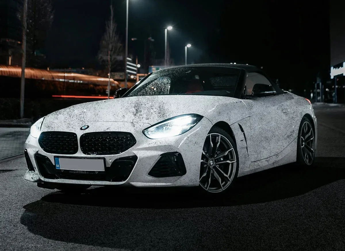 White BMW Z4 convertible on a wet street at night, headlights on.