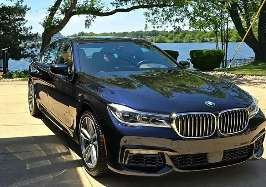 Dark blue BMW sedan parked near a body of water, reflecting sunlight.