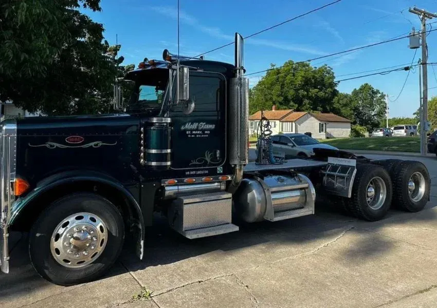 Dark green semi-truck parked on a street, with chrome accents and tall exhaust pipes.