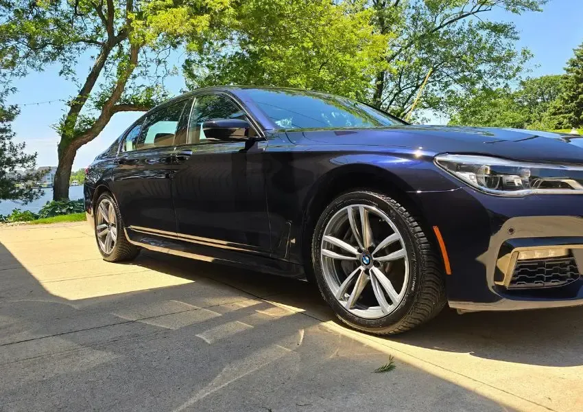 Blue BMW sedan parked on a driveway, near a lake and trees. Sunny day.
