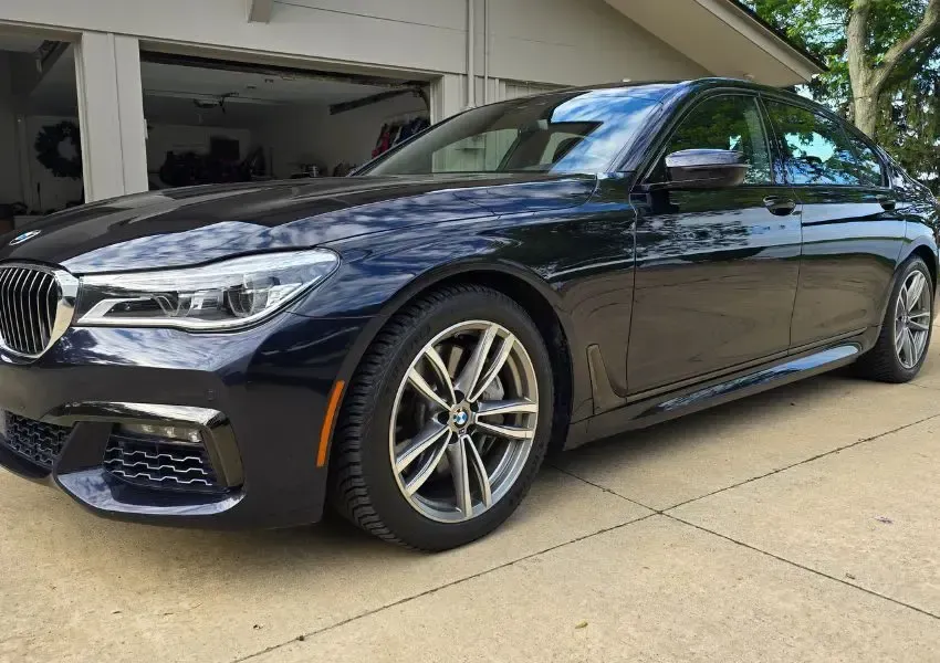 Dark blue BMW sedan parked on a concrete driveway in front of a garage.
