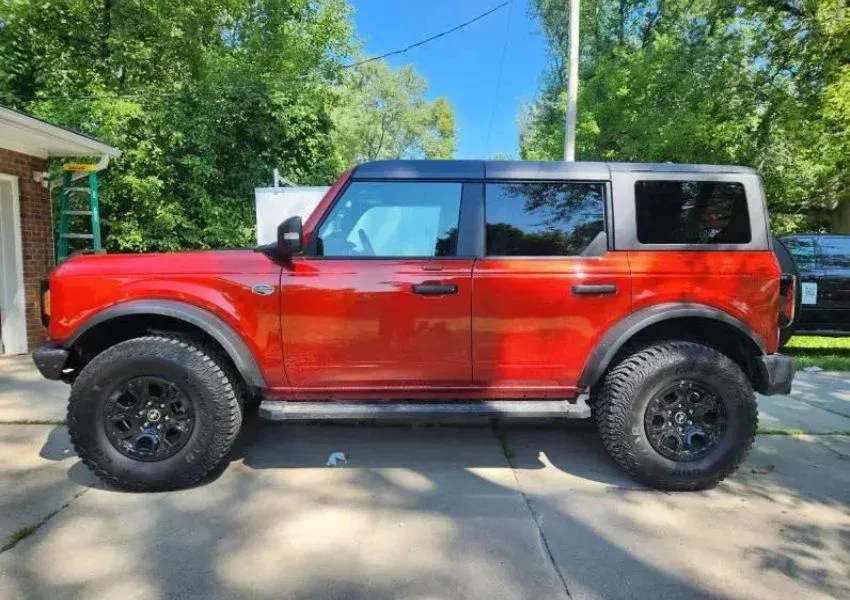 Red Ford Bronco parked on a driveway, black wheels and accents, sunny day.