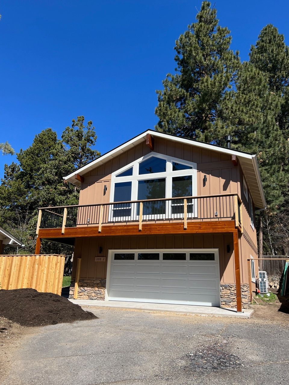 Two-story stucco house with a garage, deck, and large windows.  Brown and white exterior. Set in a wooded area.