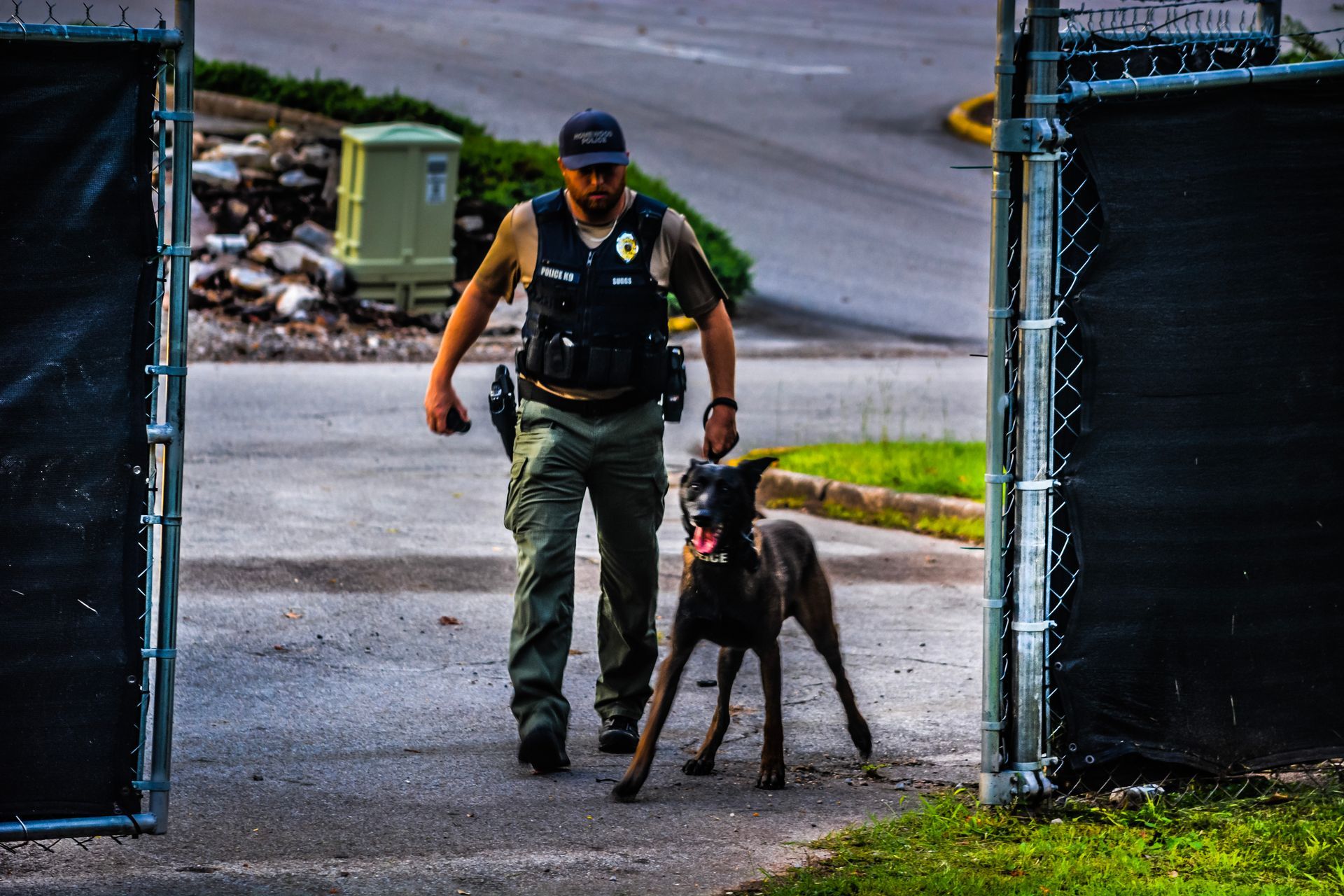 A police officer walking a dog in front of a chain link fence