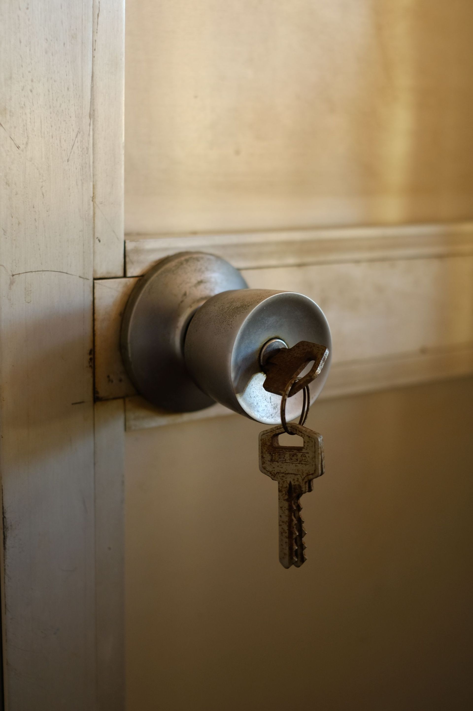 Close-up of a silver door knob with a key inserted in a beige hallway door.