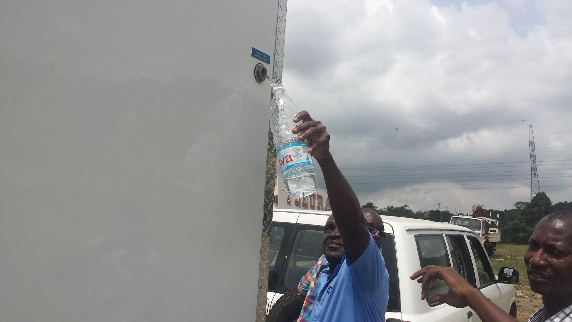 A man is holding a bottle of water in front of a white wall.