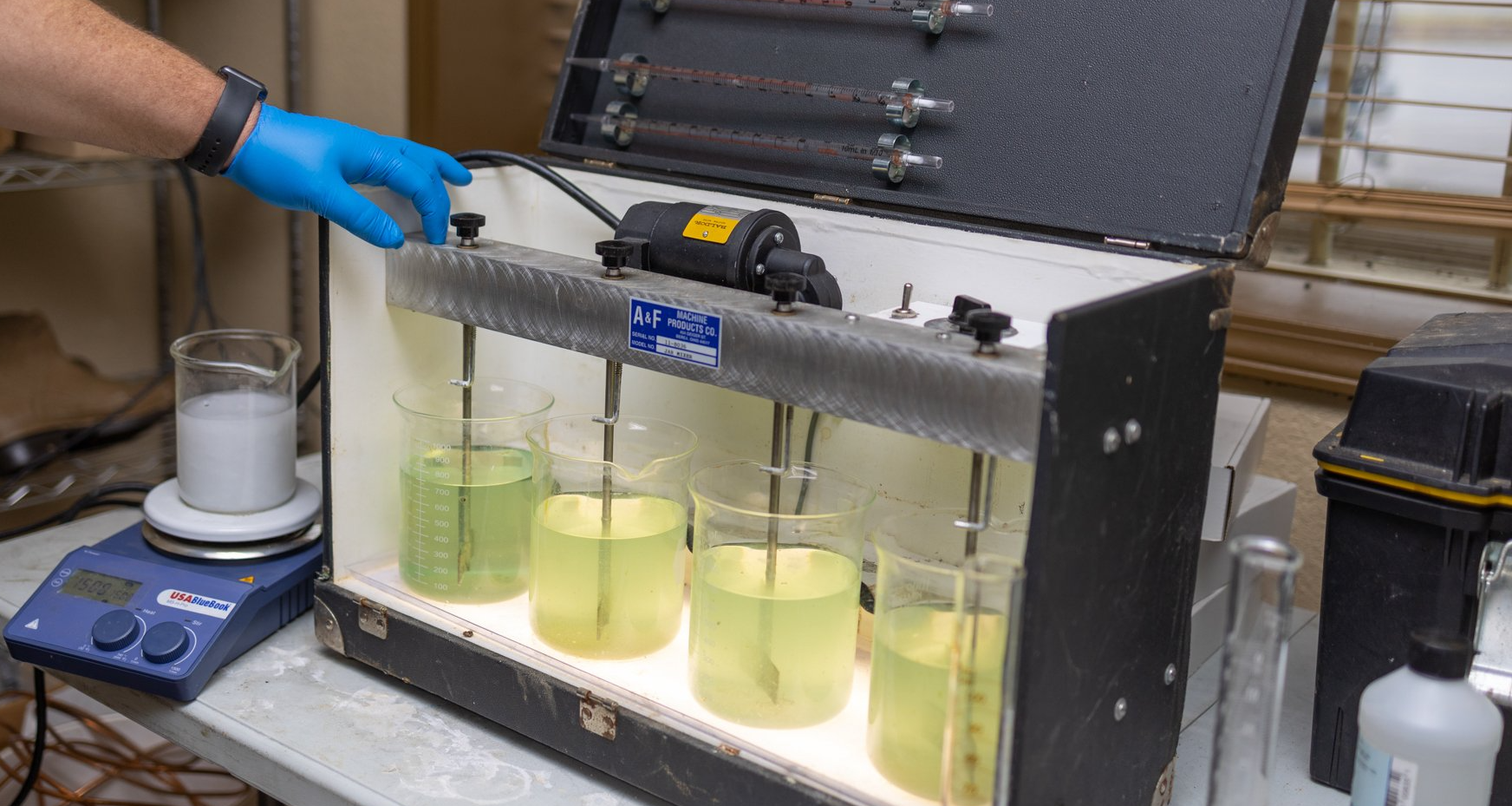 A person wearing blue gloves is working on a machine in a lab.