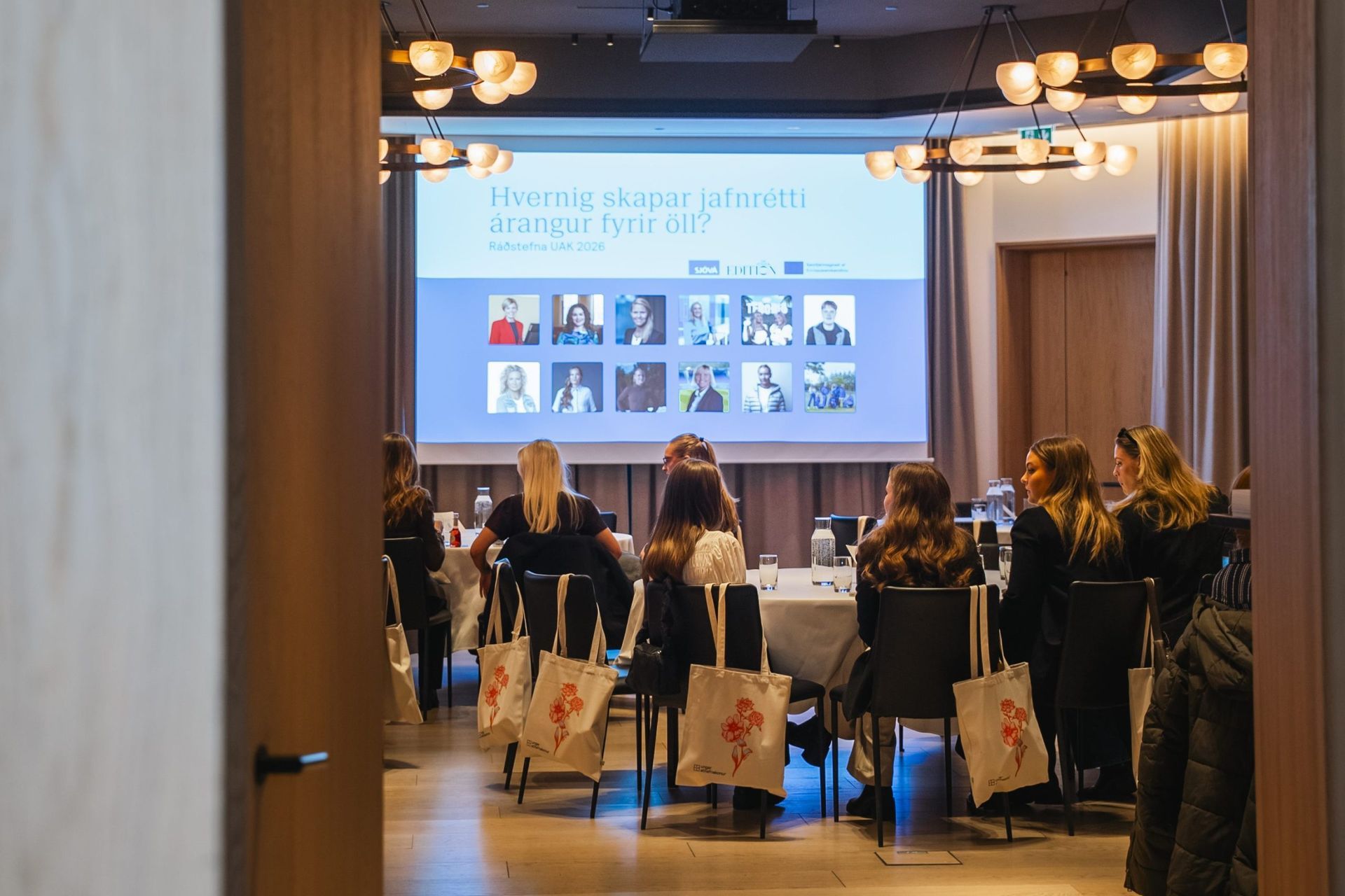Fundarherbergi með fólki sem situr við hringborð og horfir á kynningarskjá