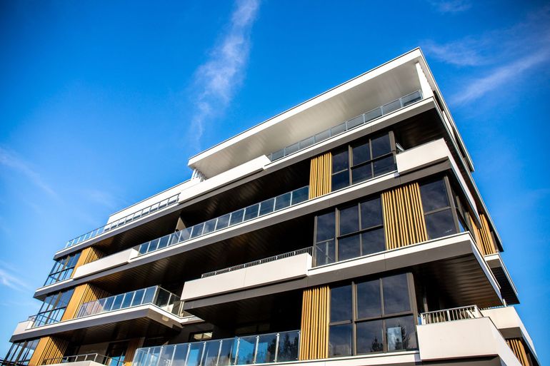 Modern multi-story building with dark glass balconies and gold accents against a blue sky