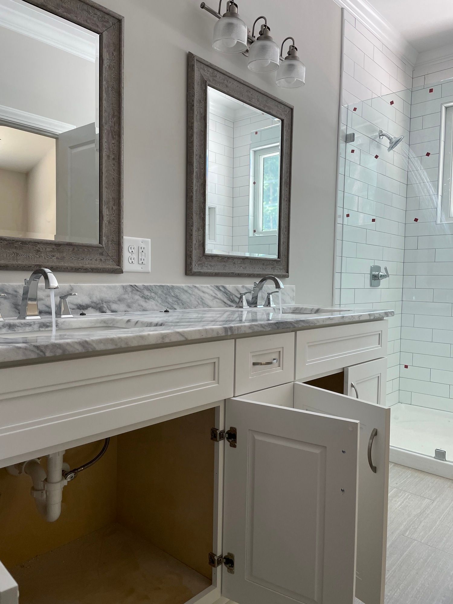 A bathroom with two sinks , two mirrors , and a walk in shower.