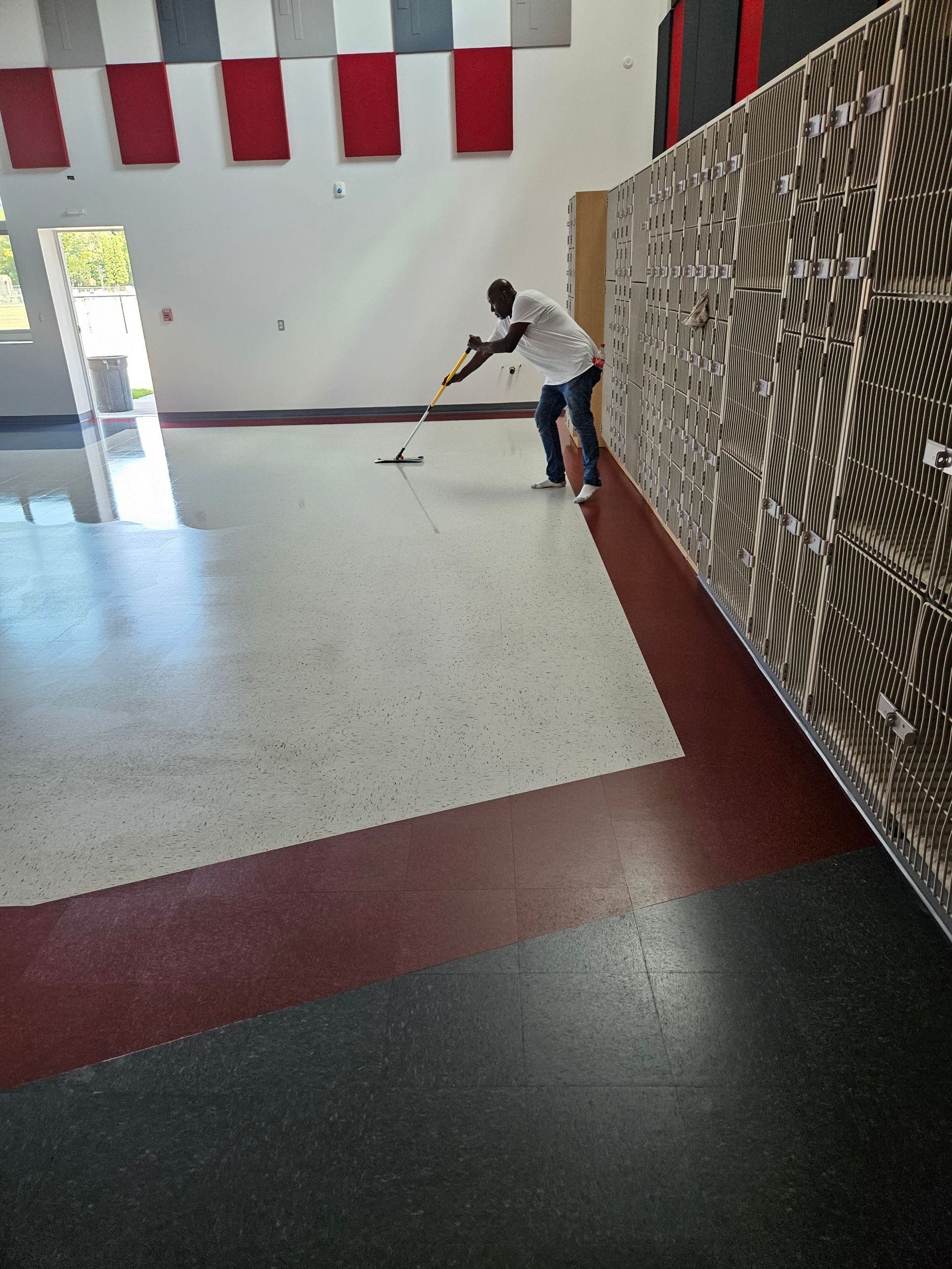 A flat mop cleaning a wooden office floor with a yellow caution sign in the background.