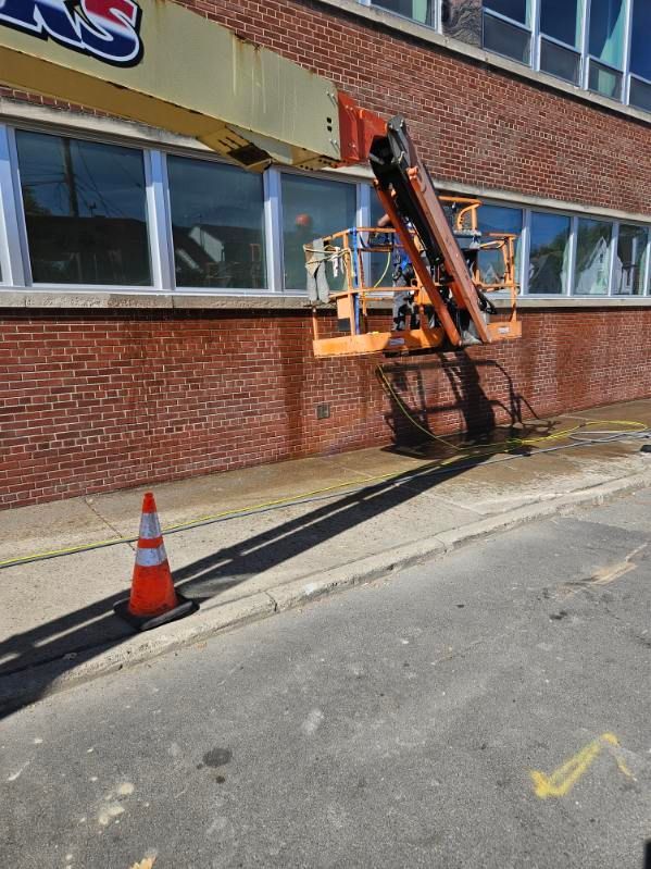 A person wearing rubber boots spreads wet concrete on a surface using a long-handled tool.