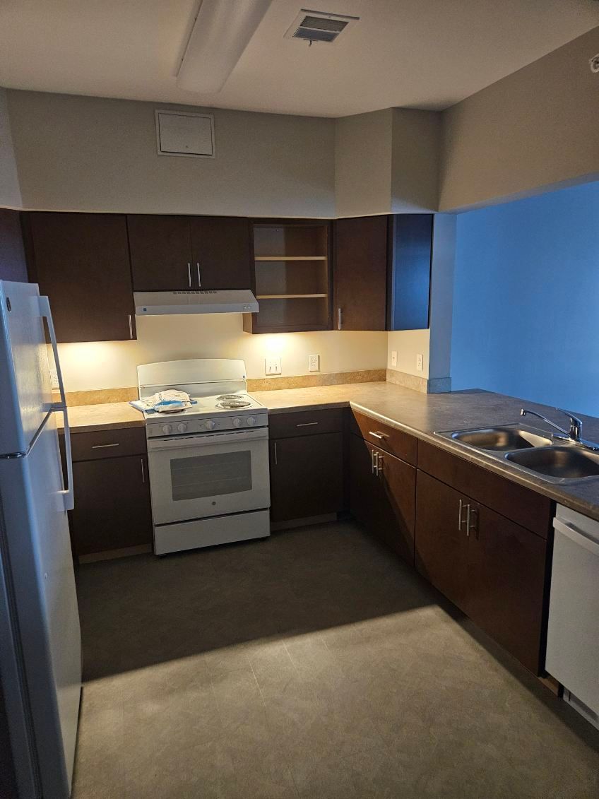 A wide shot of a modern, clean, professional stainless steel commercial kitchen with appliances and workstations.