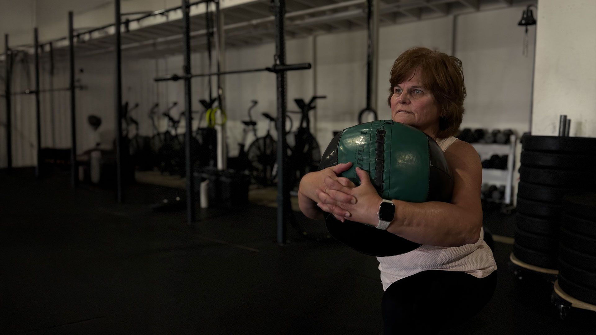 Person in Ascent CrossFit in Hesperia, CA holding a green medicine ball near a wall of hanging exercise bikes.