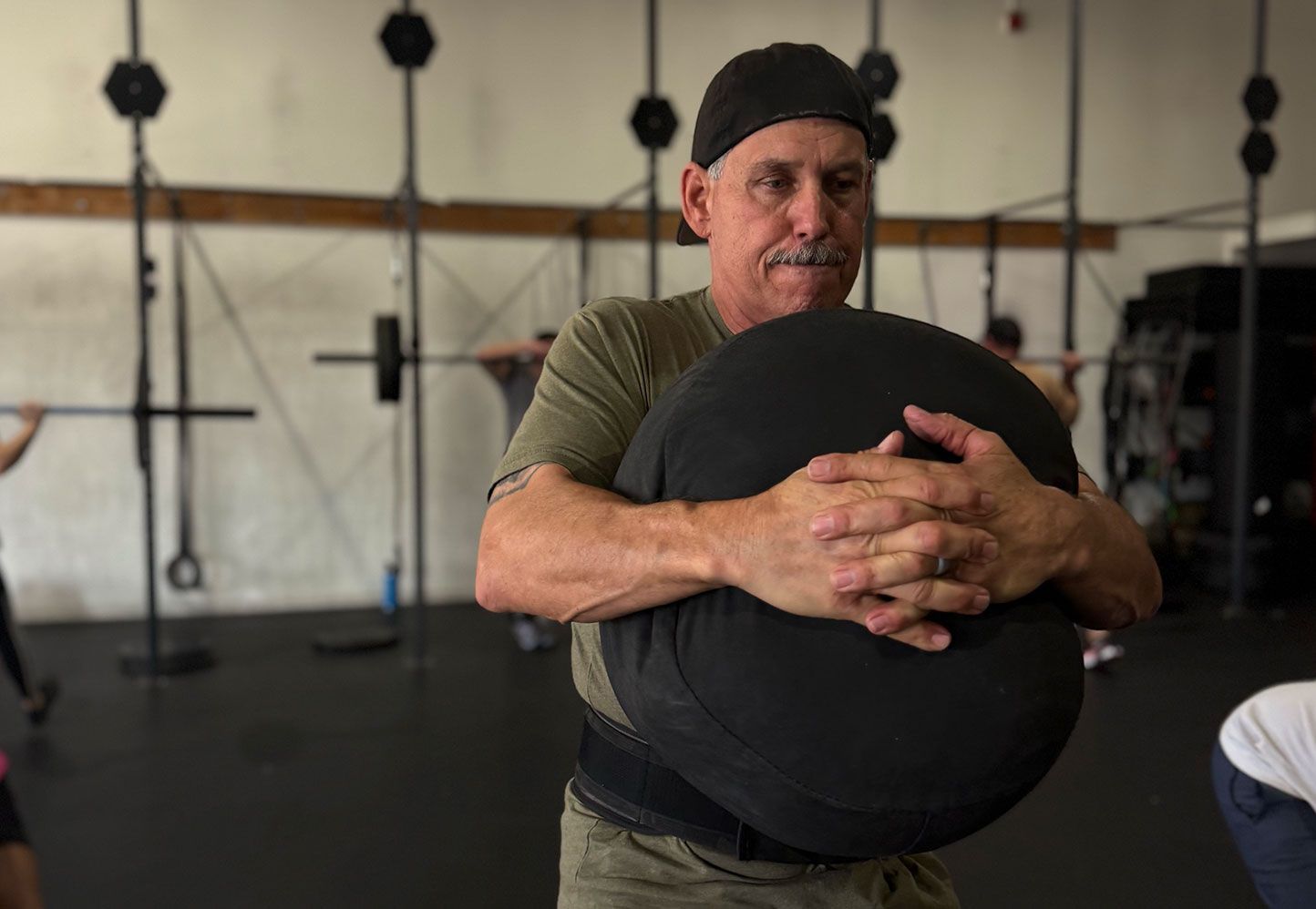 Man holding a large black exercise ball in Ascent CrossFit in Hesperia, CA, with workout equipment in the background