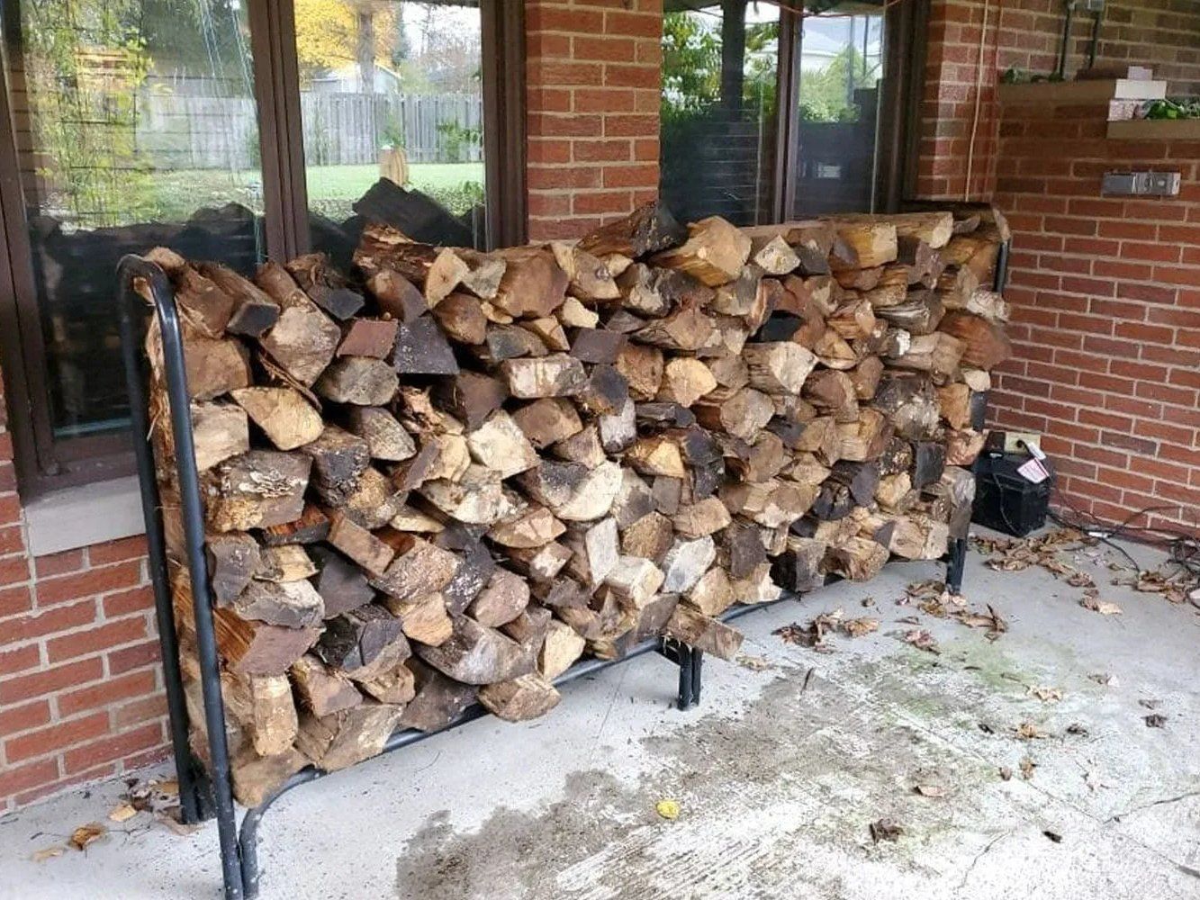 Seasoned firewood neatly stacked on a metal rack on a patio beside a brick house