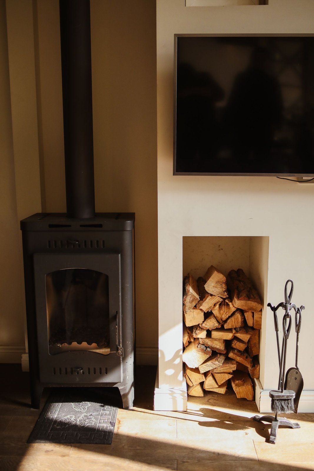 Wood-burning stove in a living room with split firewood stacked in a wall niche
