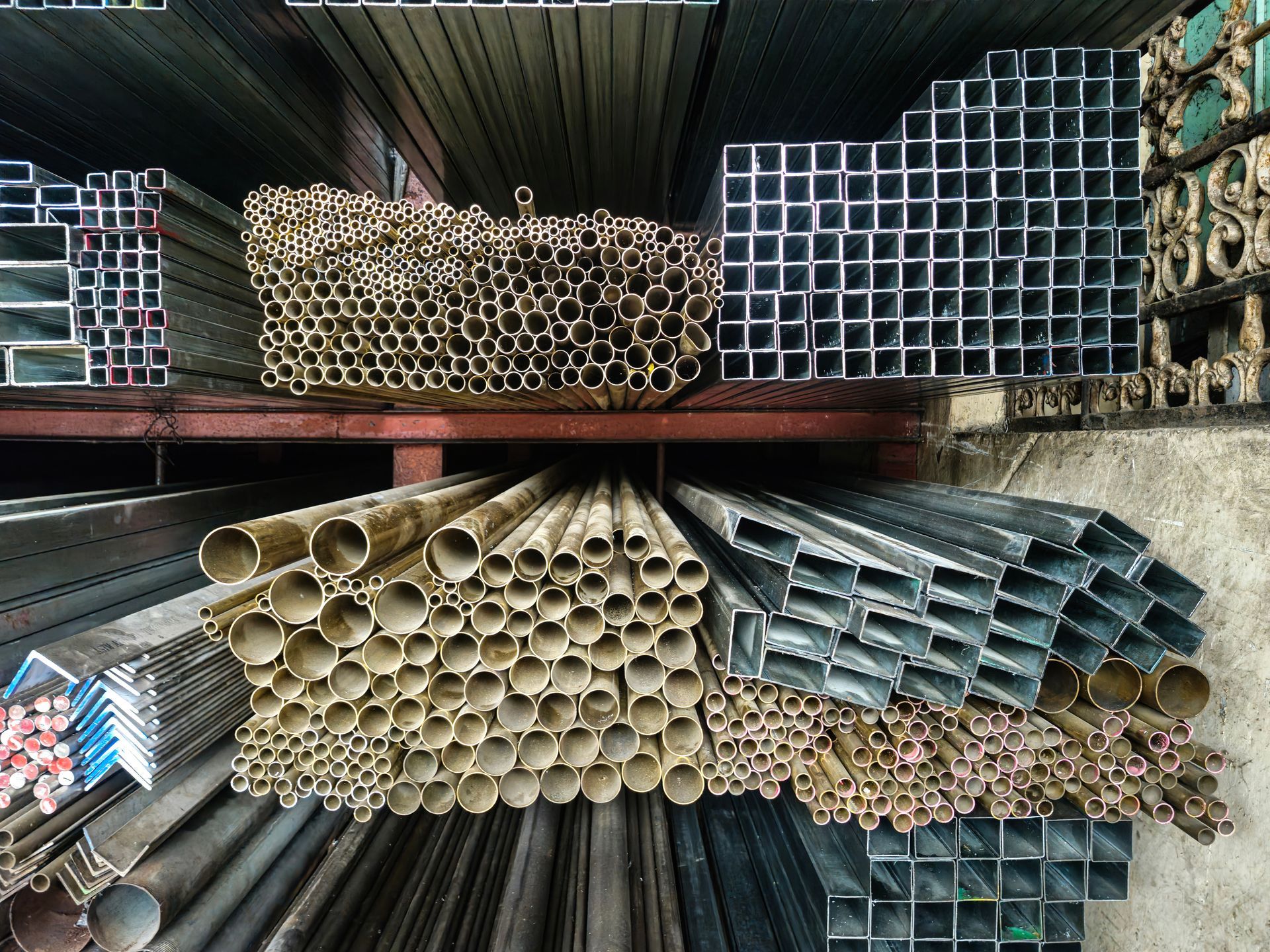 Stacked steel tubing, pipe, and square tube on warehouse racks for steel building supply.]