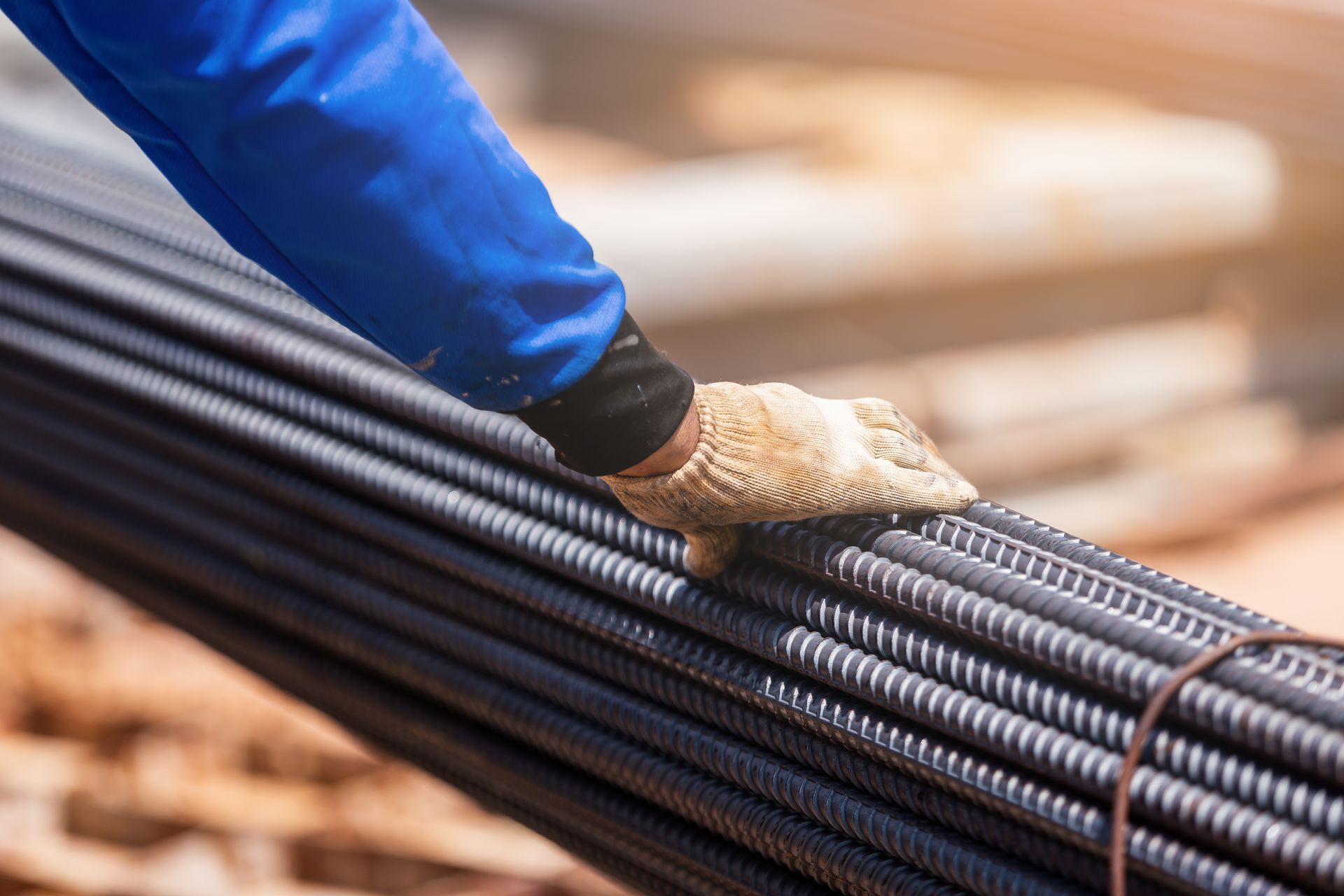Worker's gloved hand holding rebar steel bars at construction site, building materials. Worker's gloved hand holding rebar steel bars at construction site, building materials.
