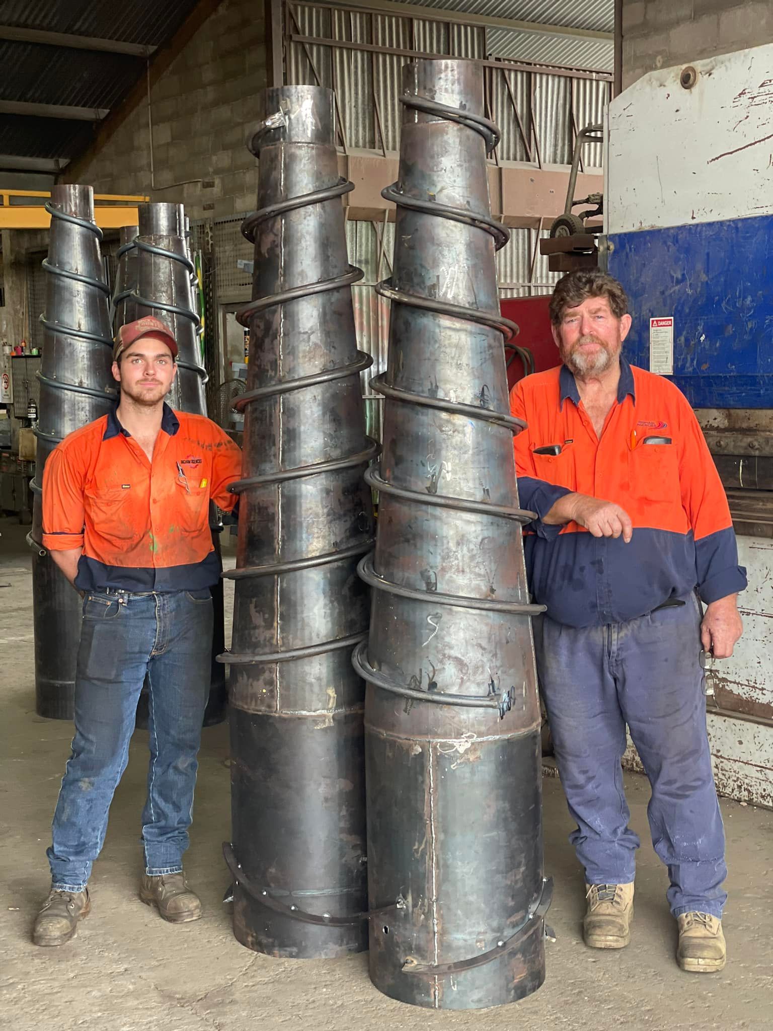 Two People in High-visibility Work Uniforms Stand Beside Two Large, Conical Metal Structures — Ingham Agencies in Ingham, QLD