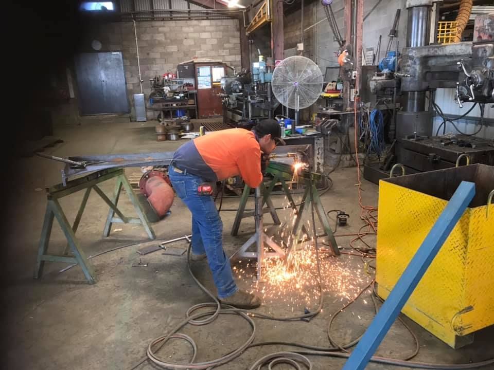 A Worker in High-visibility Orange Clothing Uses an Angle Grinder on Metal — Ingham Agencies in Ingham, QLD