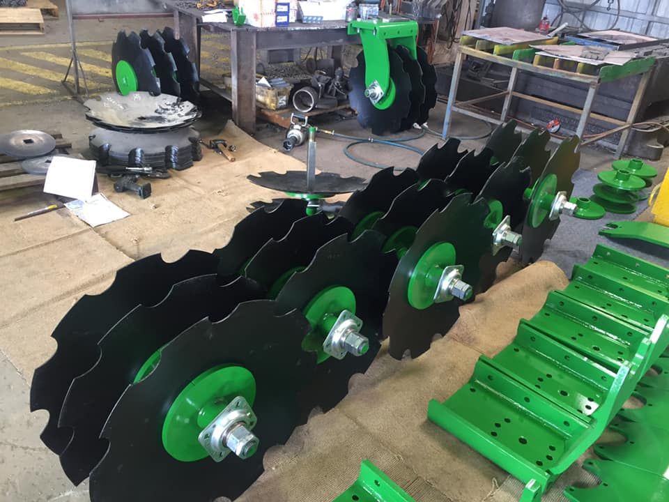 Rows of black-and-green agricultural discs and green machine parts laid out in a workshop — Ingham Agencies in Ingham, QLD