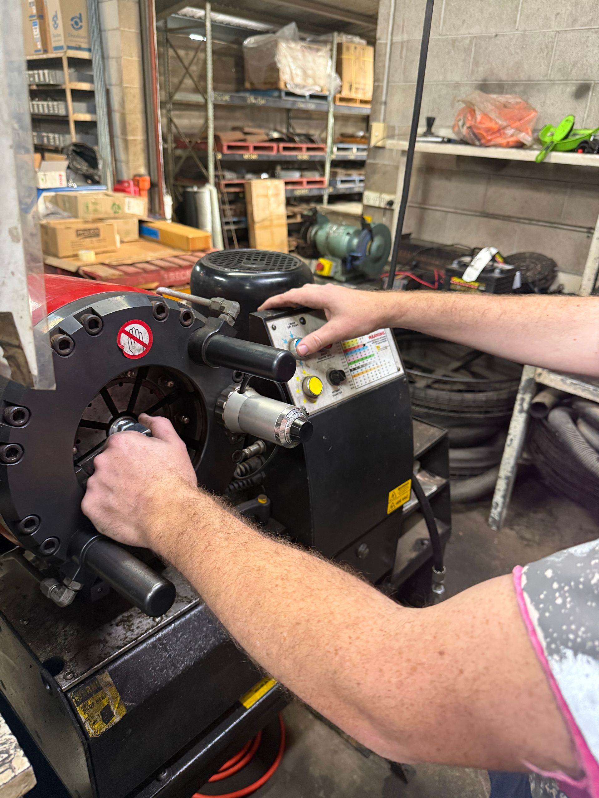 Hands operating a black machine in a workshop, with tools and shelves in the background. — Ingham Agencies in Ingham, QLD