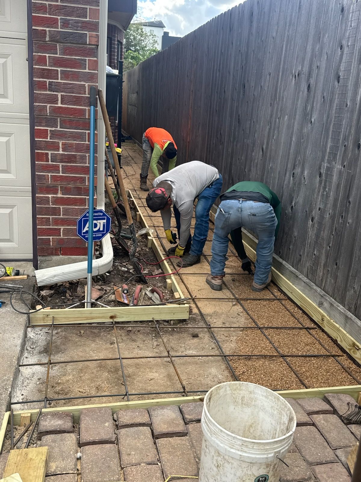 Workers installing foundation piers beside brick wall