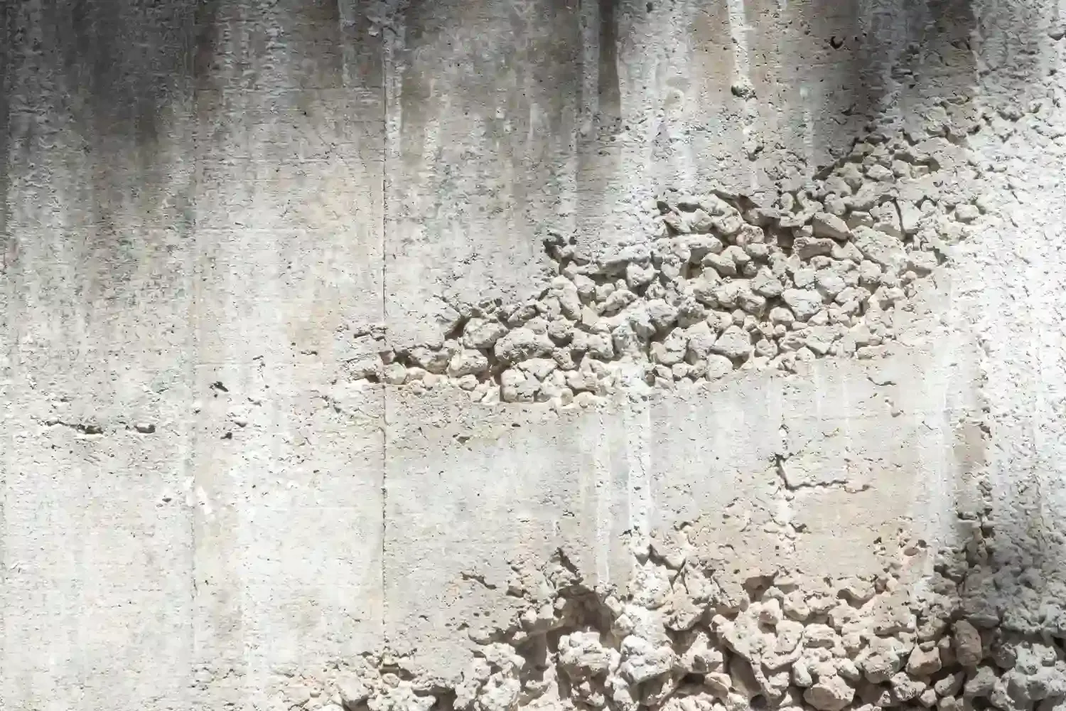 Close up of a weathered foundation wall showing what causes pitting in concrete with exposed aggregate and surface erosion