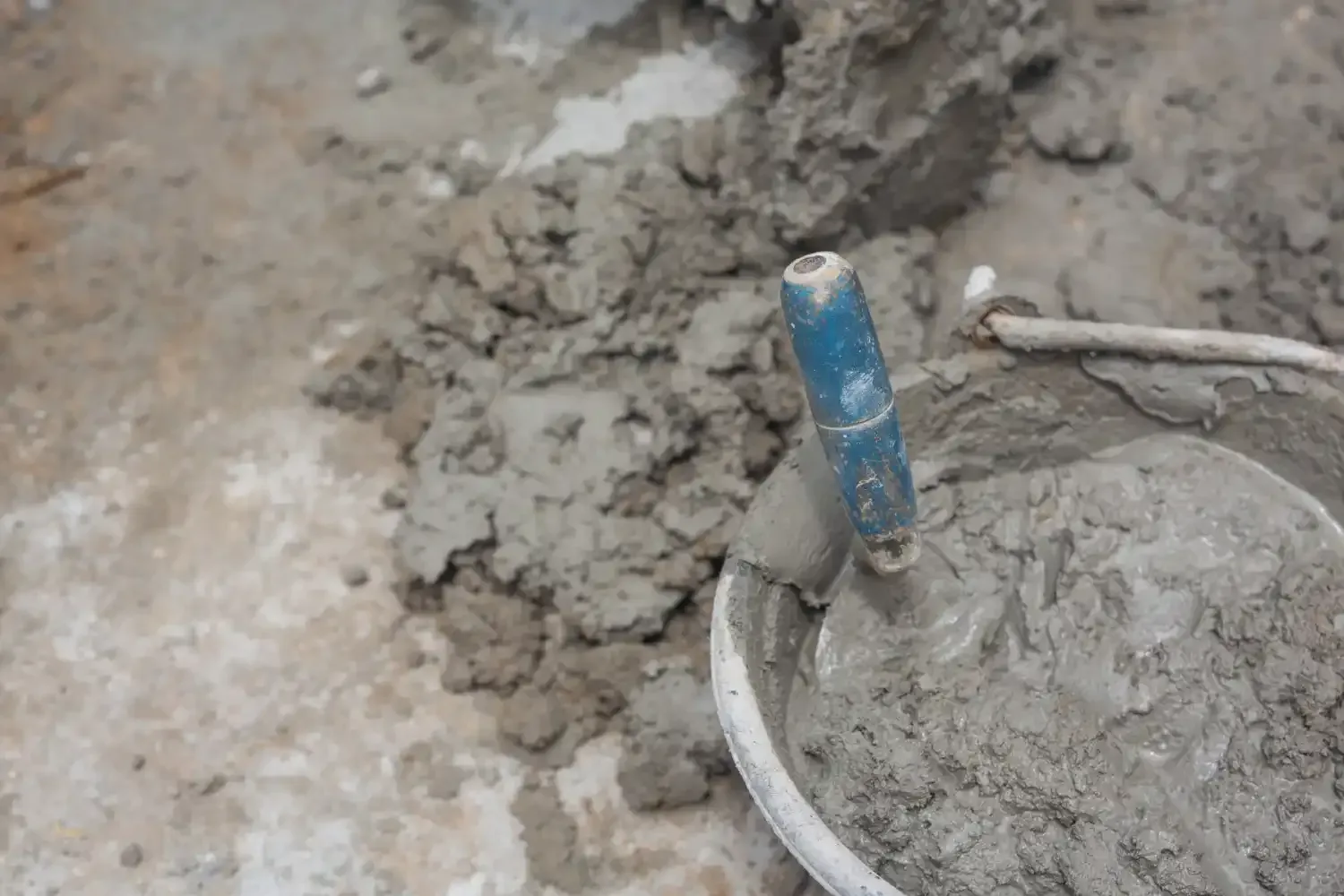 Construction worker mixing cement in a bucket to repair what causes pitting in concrete on residential foundations