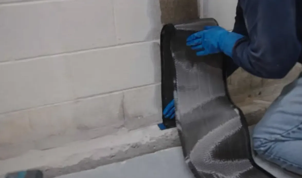 Contractor applying a carbon fiber reinforcement strip to a basement block wall by hand