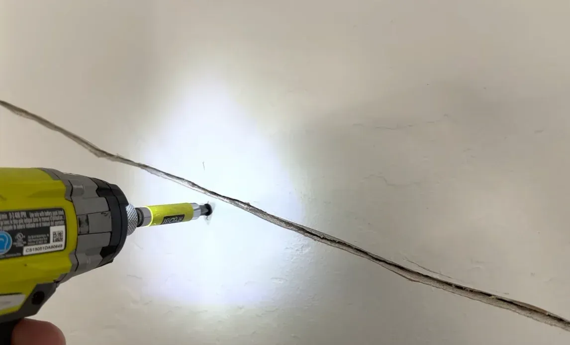 Contractor using a drill along a long diagonal wall crack during wall crack repair and foundation stability assessment in a Houston home