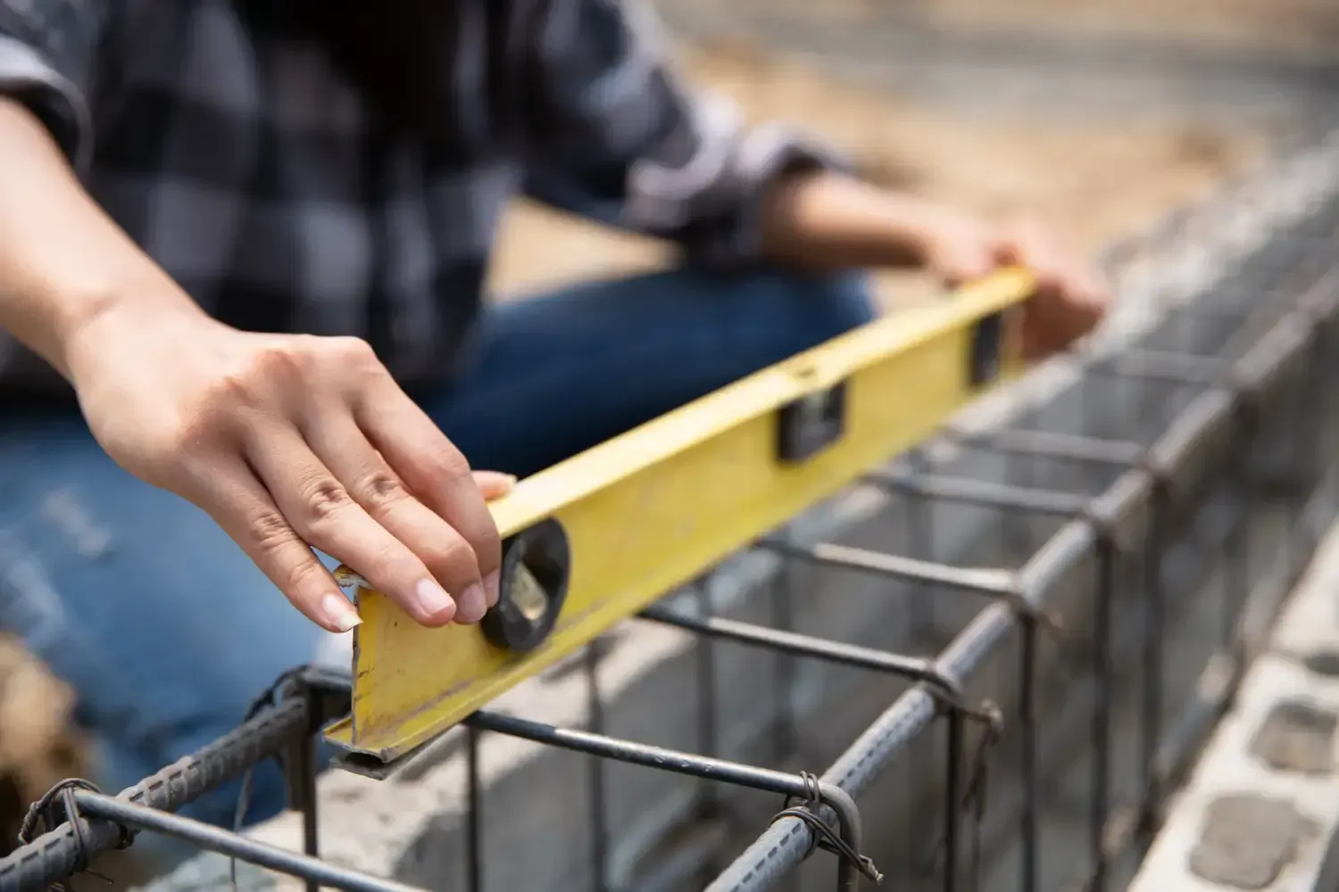 Contractor using a level on rebar footing to set a below grade foundation correctly, explaining what does below grade mean during the building process