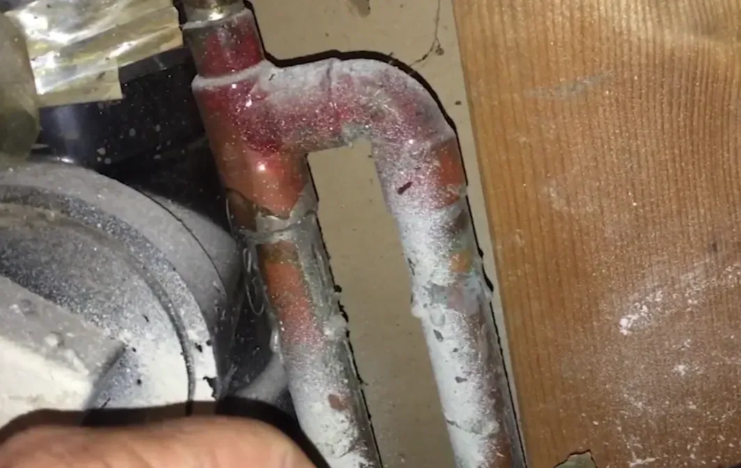 Copper water lines coated in corrosion and mineral deposits beneath a home, showing why professional slab leak repair and detection matters