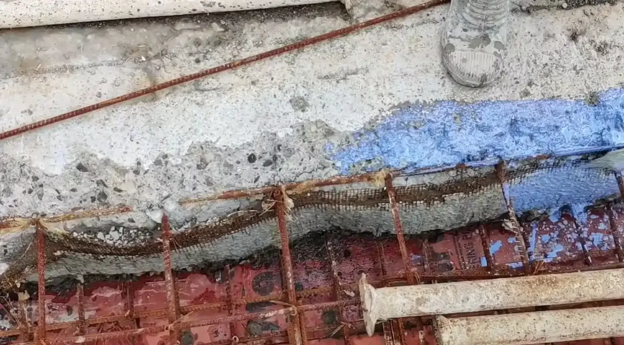 Cross-section of a construction joint in concrete showing exposed rebar reinforcement and waterproof sealant applied at the joint connection