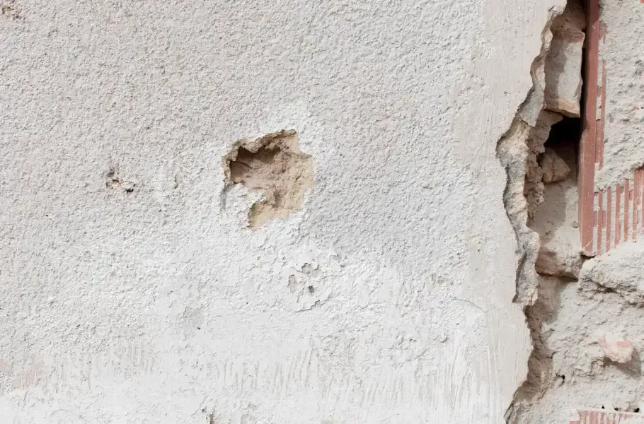 Crumbling stucco and exposed brick revealing structural foundation damage on a home