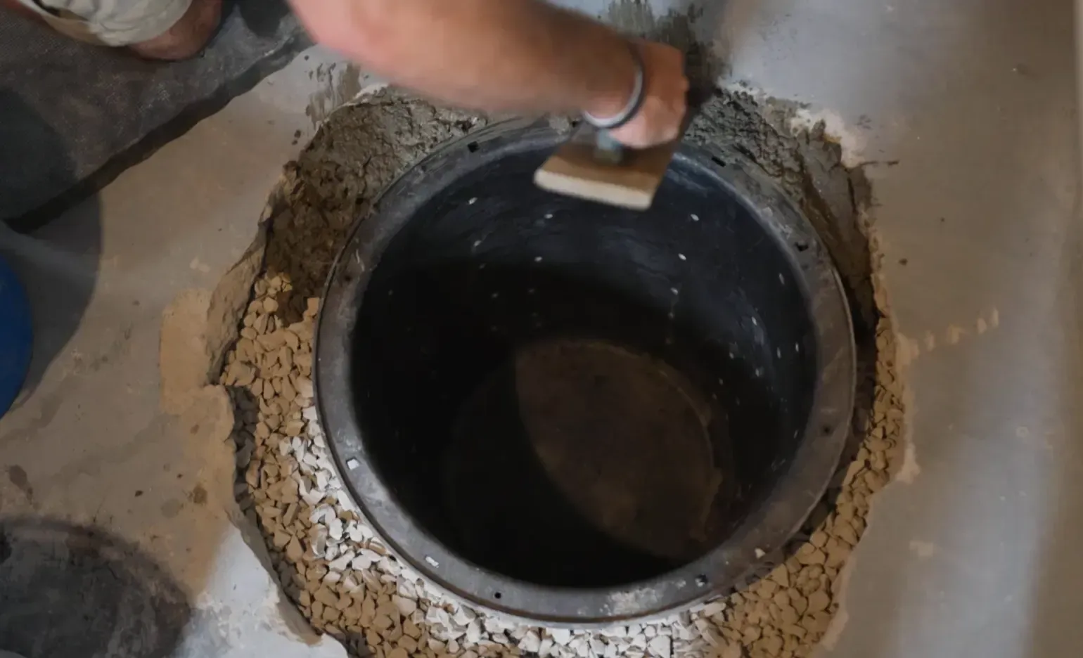 Foundation repair technician installing what is sump pit basin into concrete floor with gravel drainage