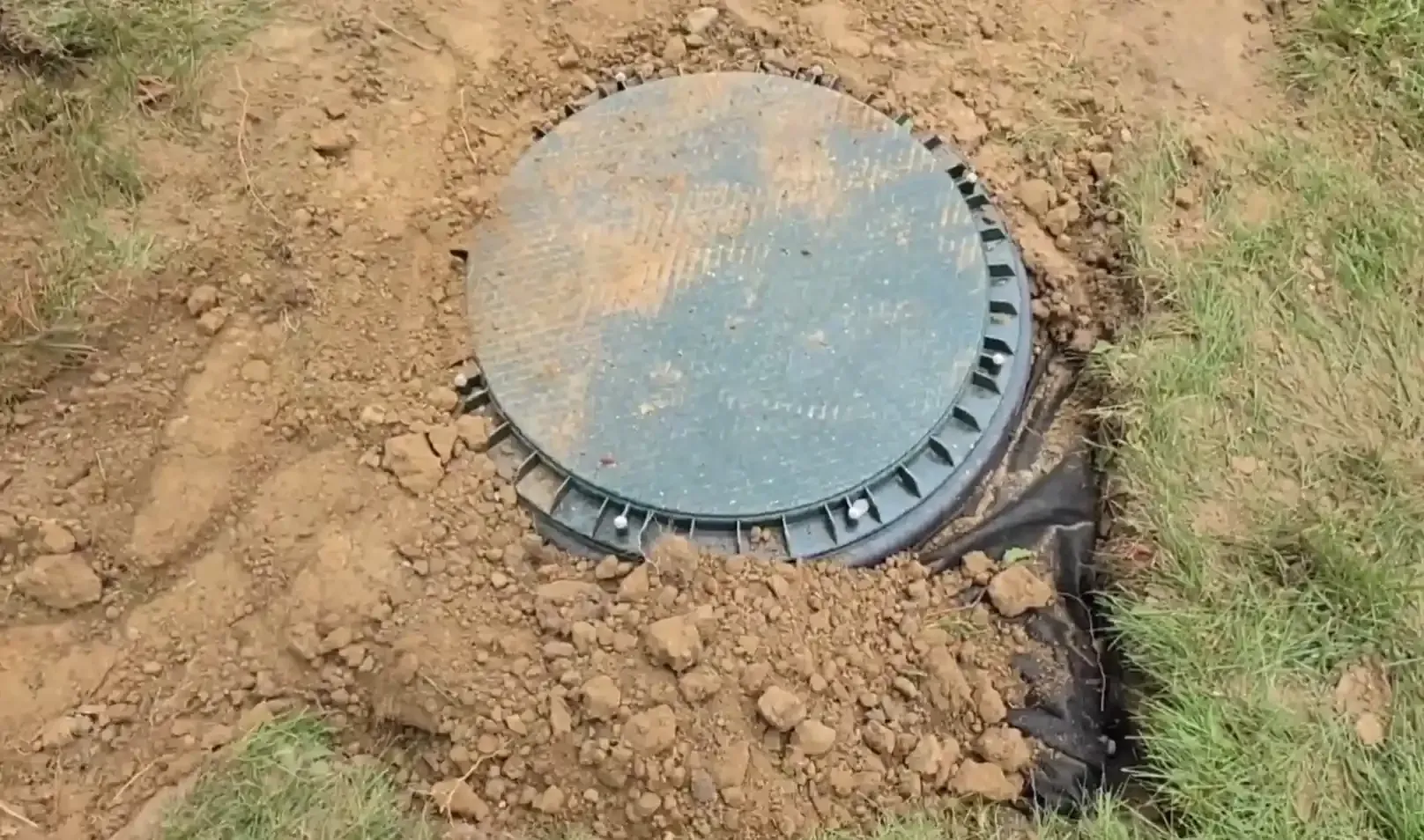 Green lid of a sump pump dry well installed in the ground for foundation drainage