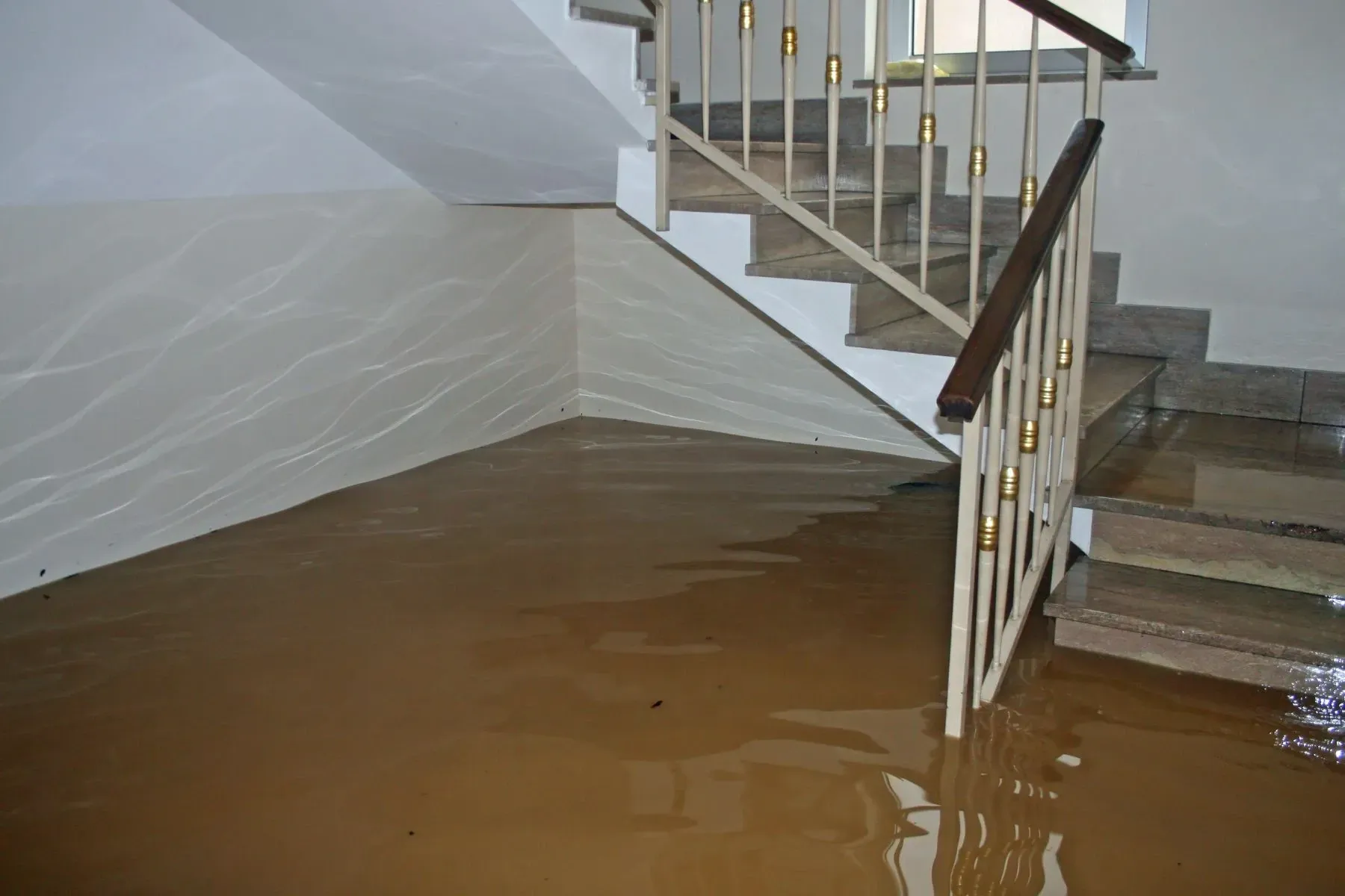 Flooded basement interior with murky standing water covering the floor near a staircase after heavy rainfall.
