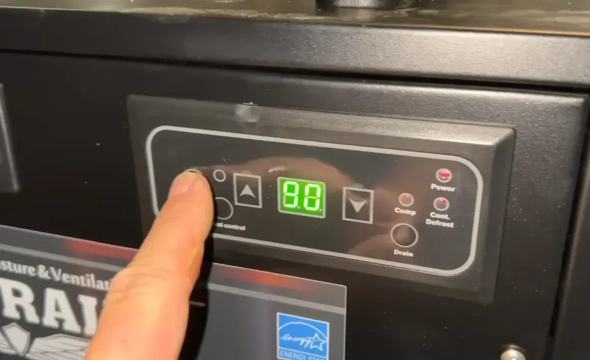 Homeowner setting the humidity level on a digital control panel, showing how crawl space dehumidifiers regulate moisture below the home