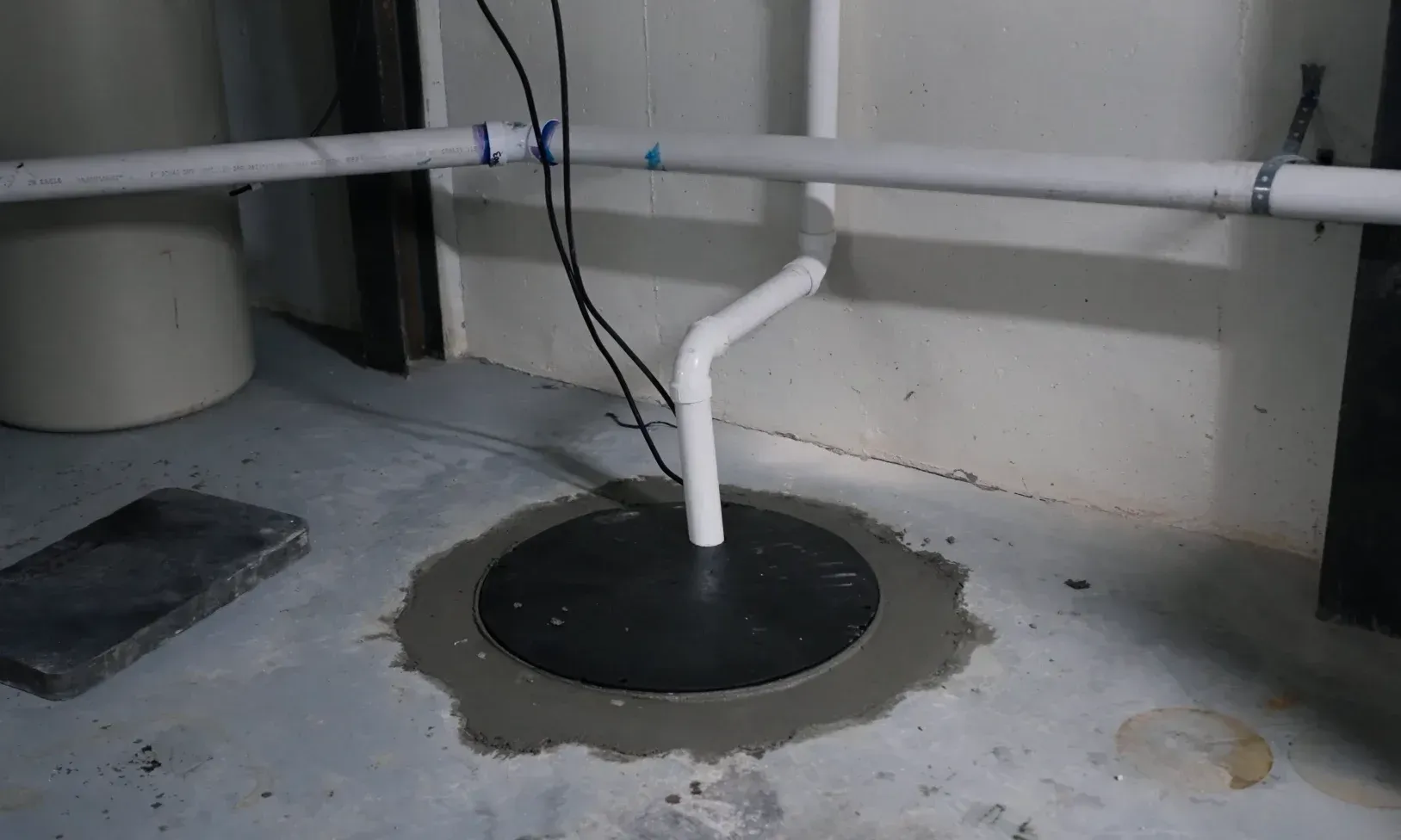 Installed sump pit with discharge pipe and sealed cover showing what is sump pit in a Houston basement