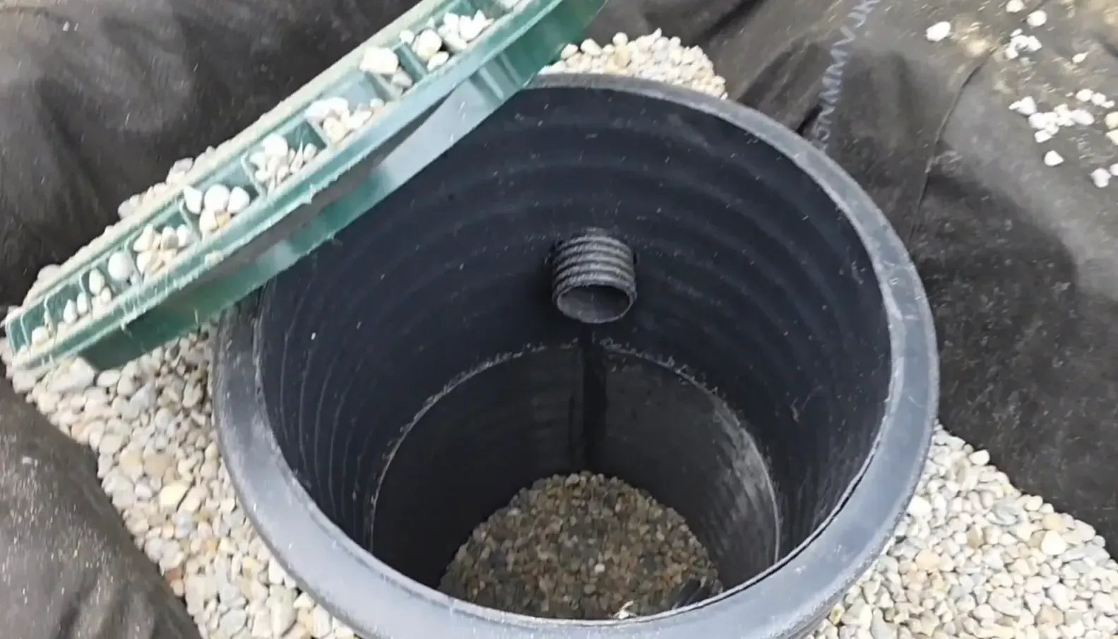 Internal view of a sump pump dry well basin with a drainage pipe and gravel base