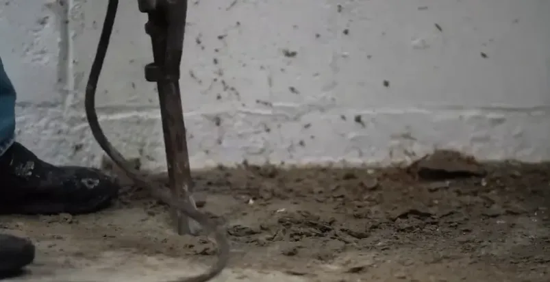 Jackhammer breaking through concrete to excavate a sump pit in basement floor during foundation drainage installation