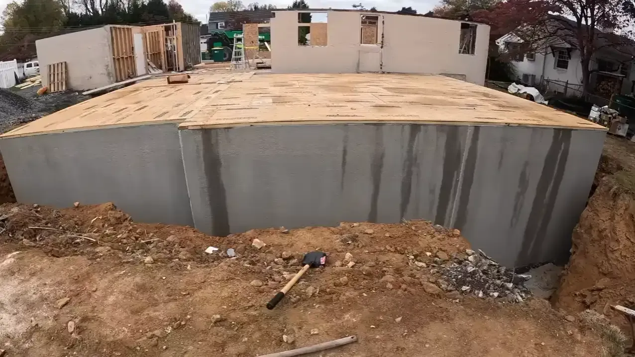 Open excavation trench around a waterproofed concrete foundation showing what is backfill in construction before soil is replaced