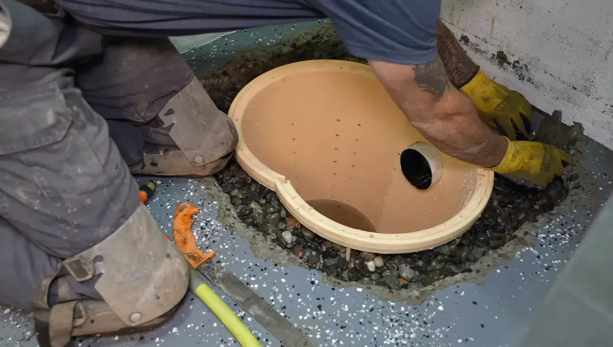 Plumber fitting a perforated sump basin into a gravel bed during a basement sump pit design installation