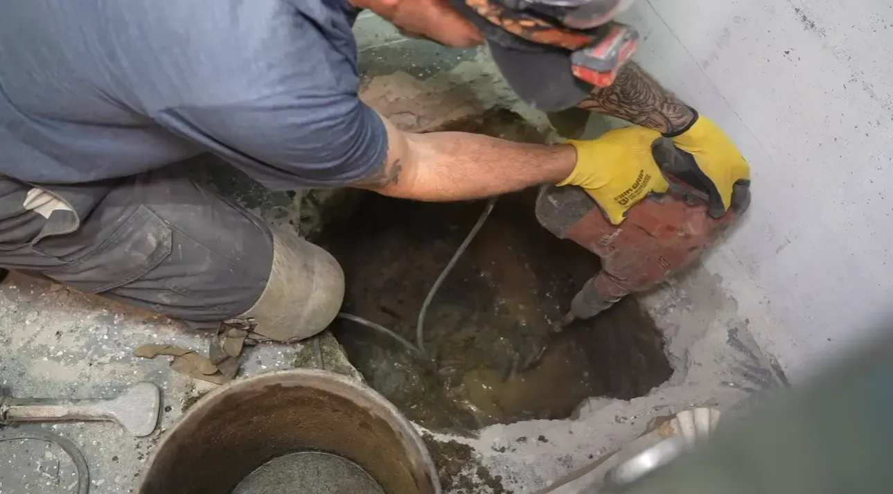 Technician using a hammer drill to excavate a new sump pit in a basement concrete floor