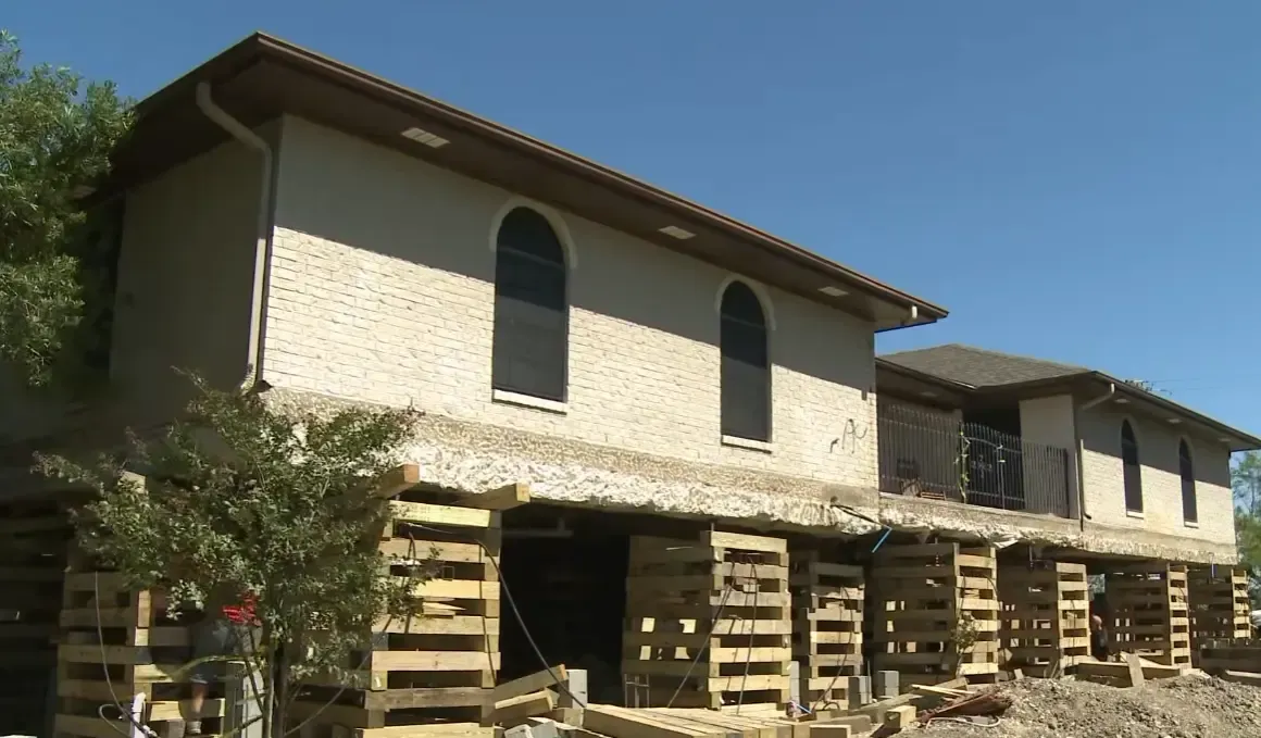 Two story brick home elevated on wooden cribbing supports showing what factors into foundation and house raising costs in Houston
