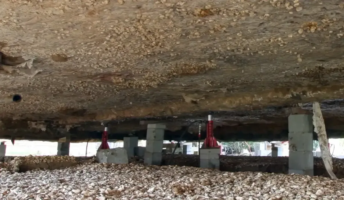 View beneath a concrete slab supported by hydraulic jacks and concrete block piers illustrating foundation and house raising costs for structural lifting projects